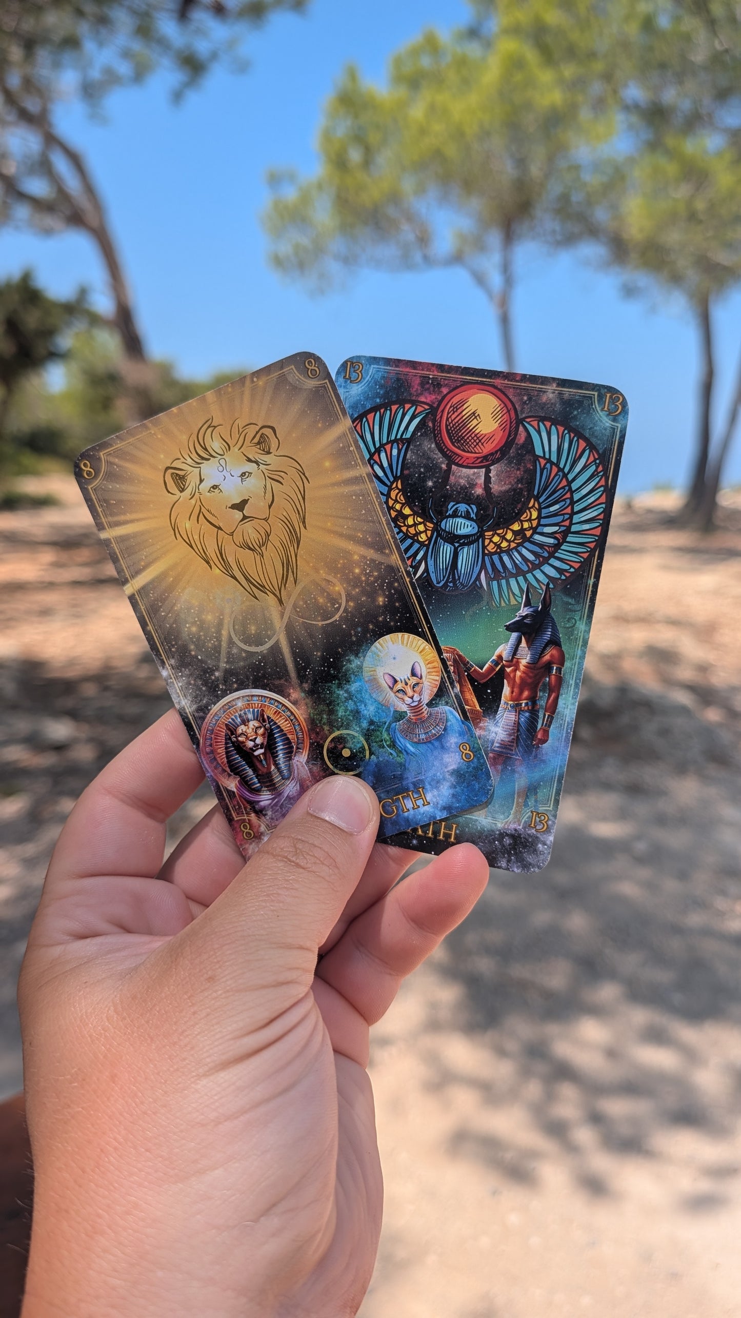 Written in the Stars Tarot cards by Emporos held in sunlight — Strength and Death Higher Arcana cards with Egyptian symbolism, Sekhem energy healing